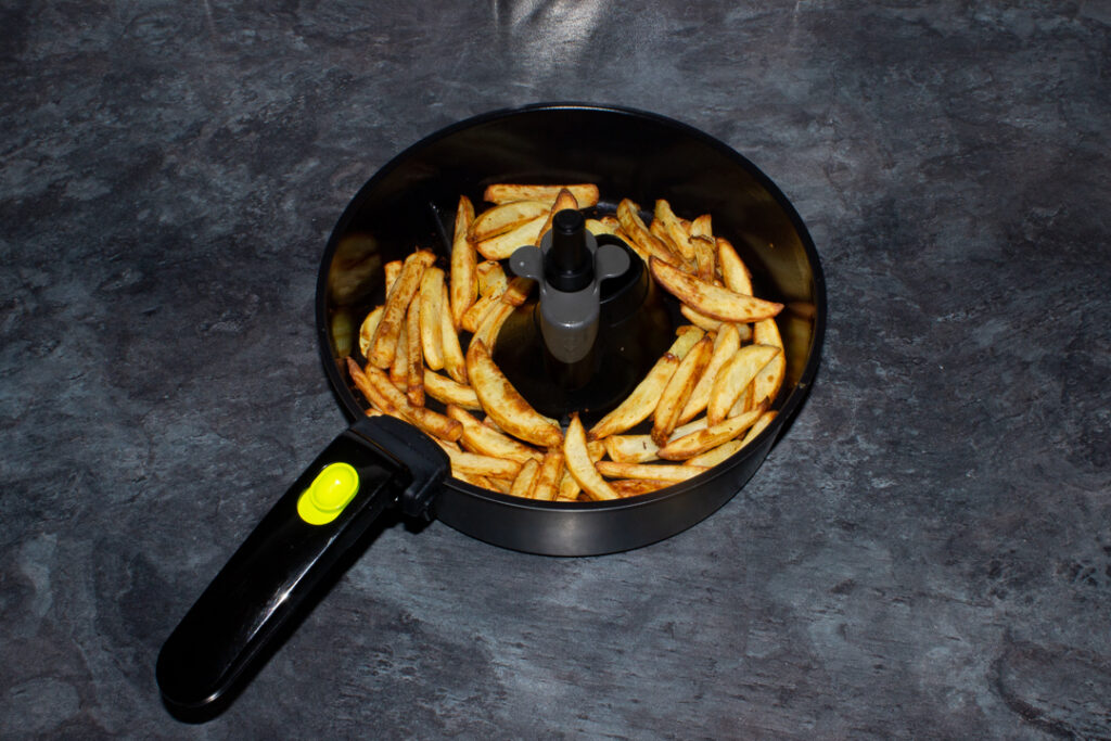 Cooked chips in an air fryer pan on a kitchen worktop.