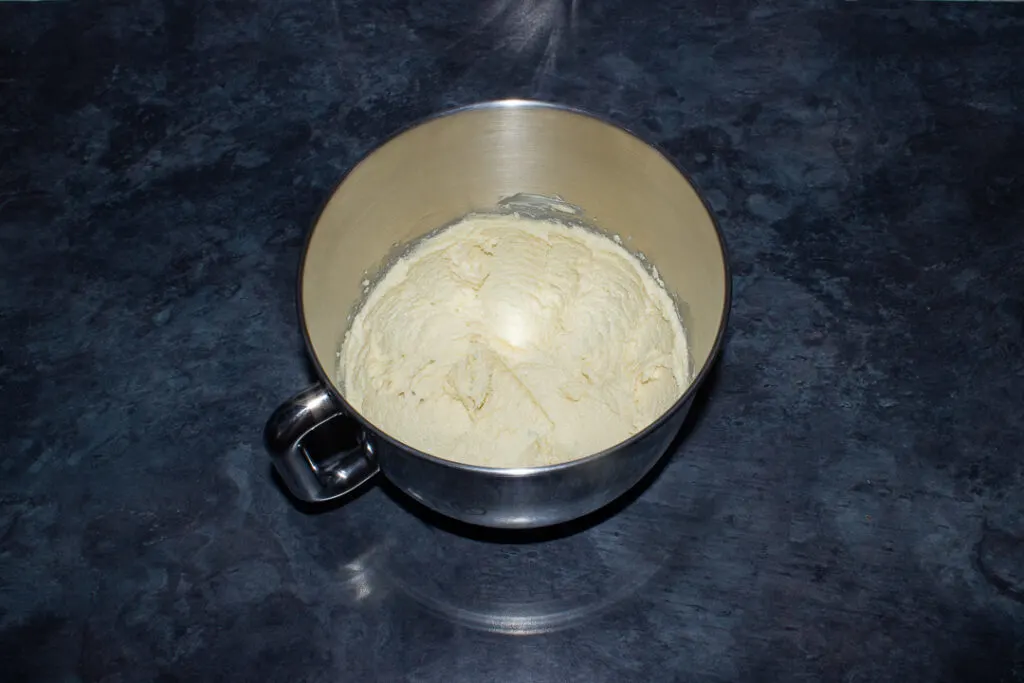 Creamed butter and sugar in the bowl of an electric stand mixer on a kitchen worktop.