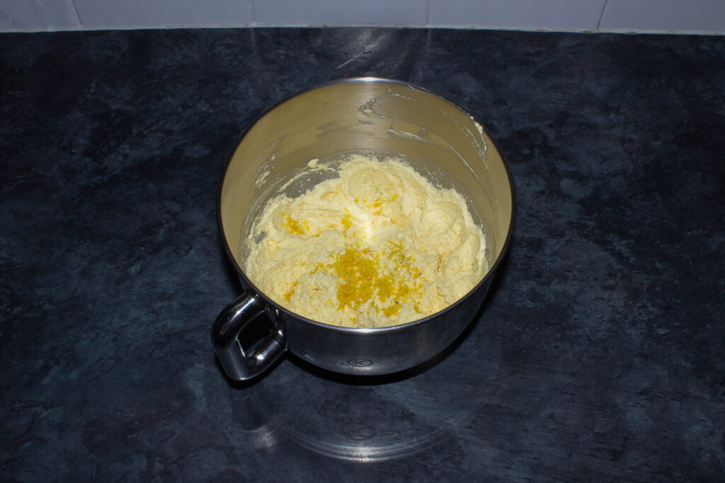 Beaten butter, sugar, eggs and lemon zest in the bowl of an electric stand mixer on a kitchen worktop.
