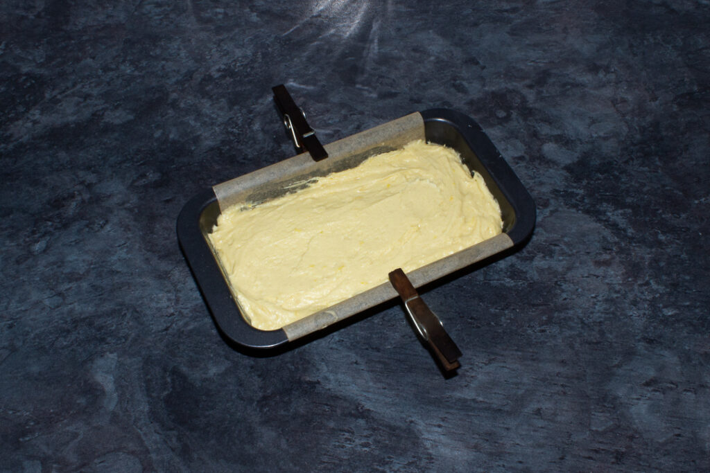 Lemon drizzle cake batter in a lined loaf pan on a kitchen worktop.
