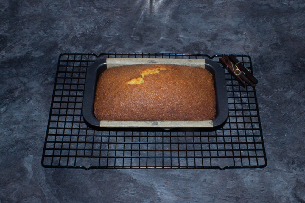A freshly baked lemon drizzle loaf cake in a tin on a wire rack.