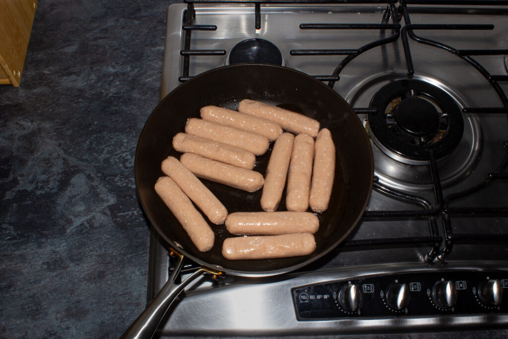 12 sausages frying in a pan on the stove.