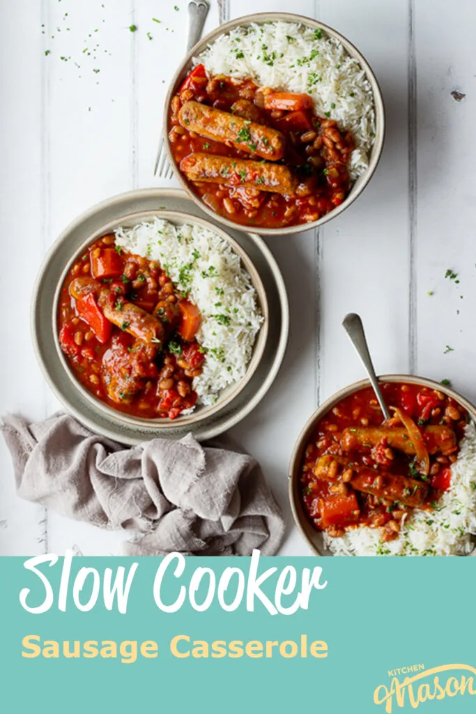 A top down view of 3 bowls filled with slow cooker sausage casserole with beans and rice. Set over a white wood effect backdrop, there are also some forks, scattered chopped parsley and a light brown linen napkin in the background. A text overlay says Slow cooker sausage casserole.