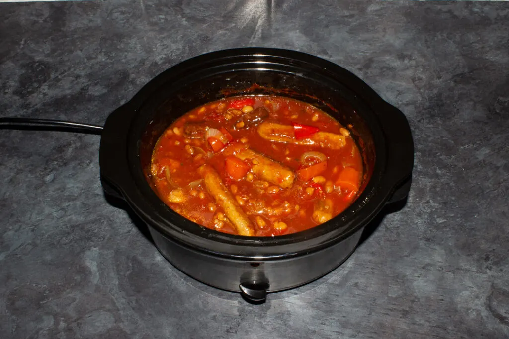 A sausage casserole with beans that has finished slow cooking in a slow cooker on a kitchen worktop.
