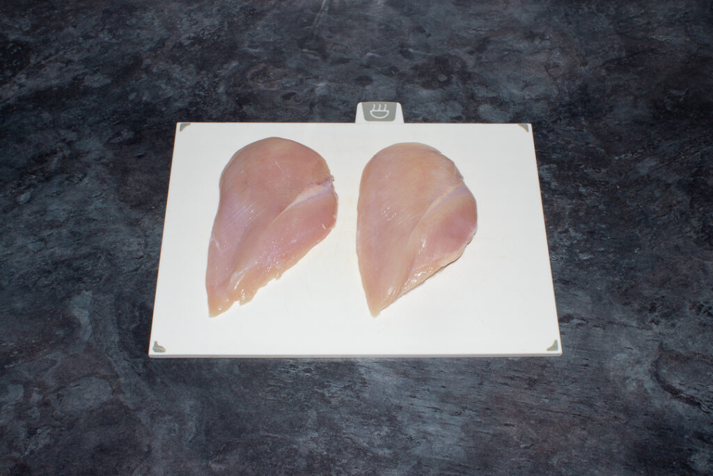 2 large chicken breasts on a white chopping board over a kitchen worktop.