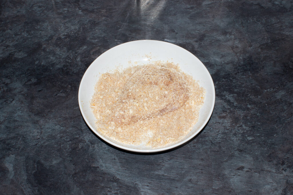 A large chicken breast in a dish of seasoned breadcrumbs.