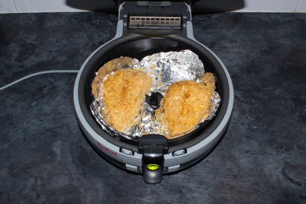 2 x cooked juicy and golden air fried chicken breasts in a foil lined air fryer.