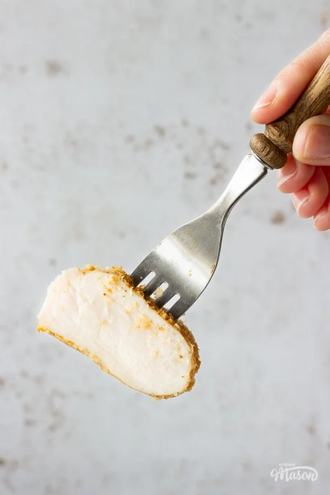 A close up shot of someone holding a piece of juicy air fried chicken breast on the end of a fork with a wooden handle.