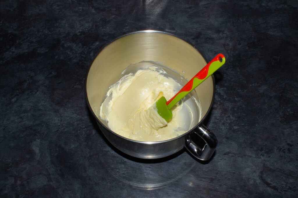 Softened butter in the bowl of an electric stand mixer with a green spatula.