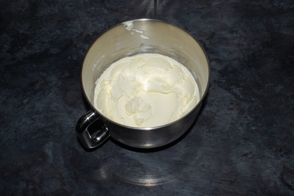 Buttercream frosting in the bowl of an electric stand mixer on a kitchen worktop.
