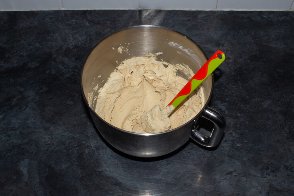 Biscoff buttercream frosting in an electric stand mixer bowl with a green spatula.