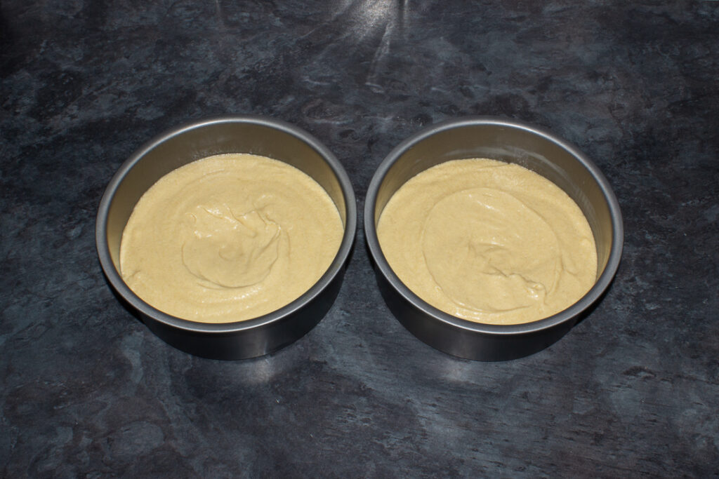 Biscoff cake batter divided between two lined cake tins on a kitchen worktop.
