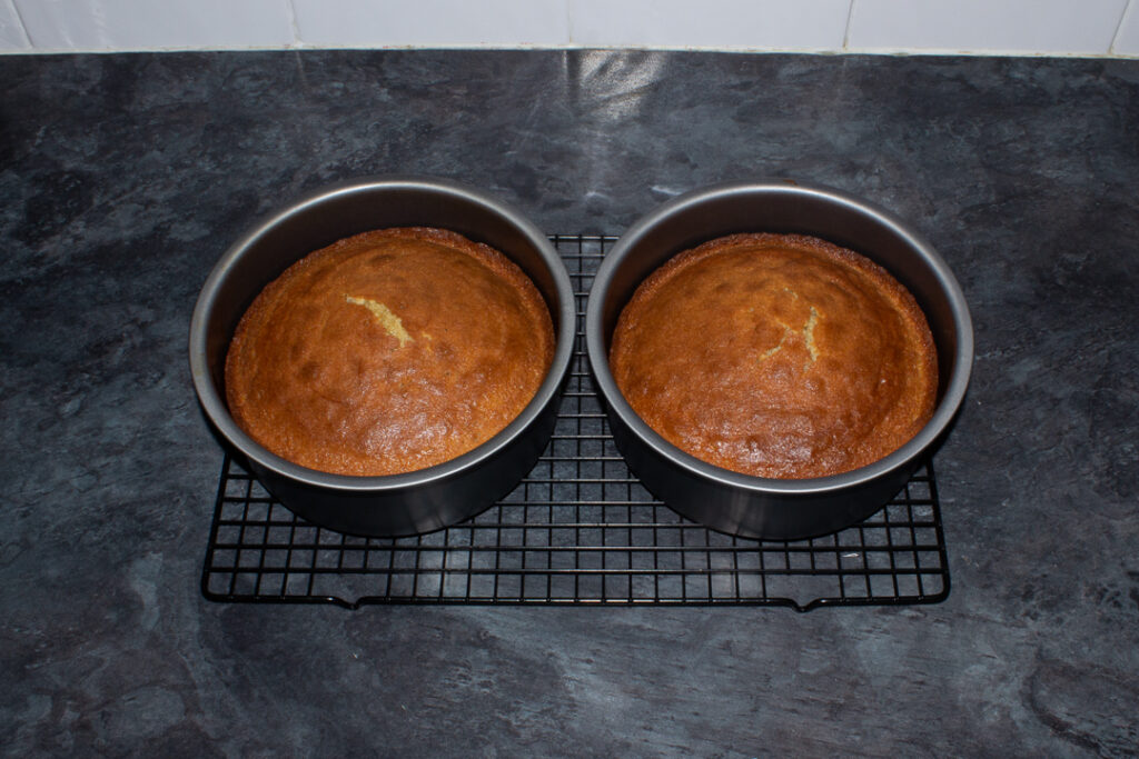 Two baked Biscoff sponge cake layers in baking tins on a cooling rack.
