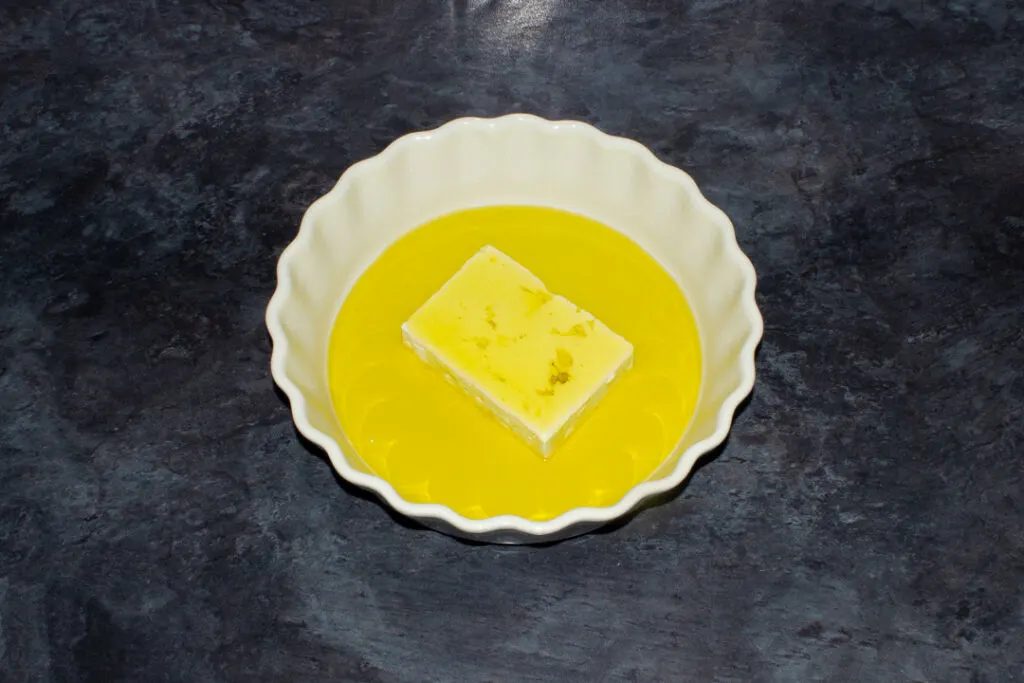 A block of feta covered in olive oil in an ovenproof dish