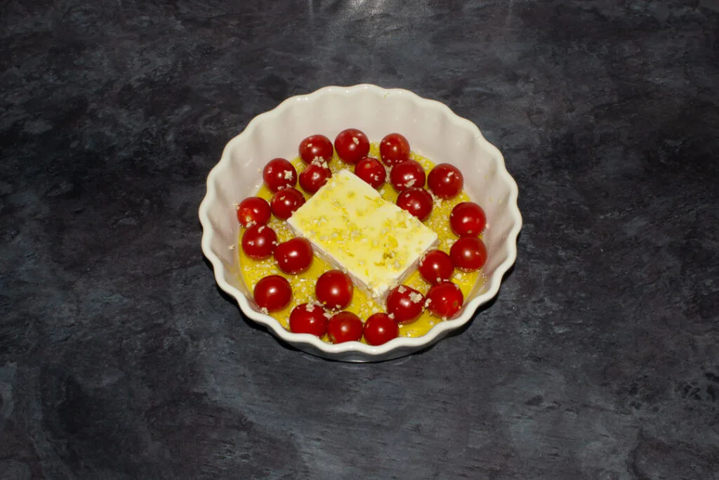 Tomatoes, a block of feta and garlic covered in olive oil in a dish