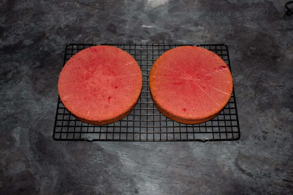 Two strawberry cakes cooling on a rack.