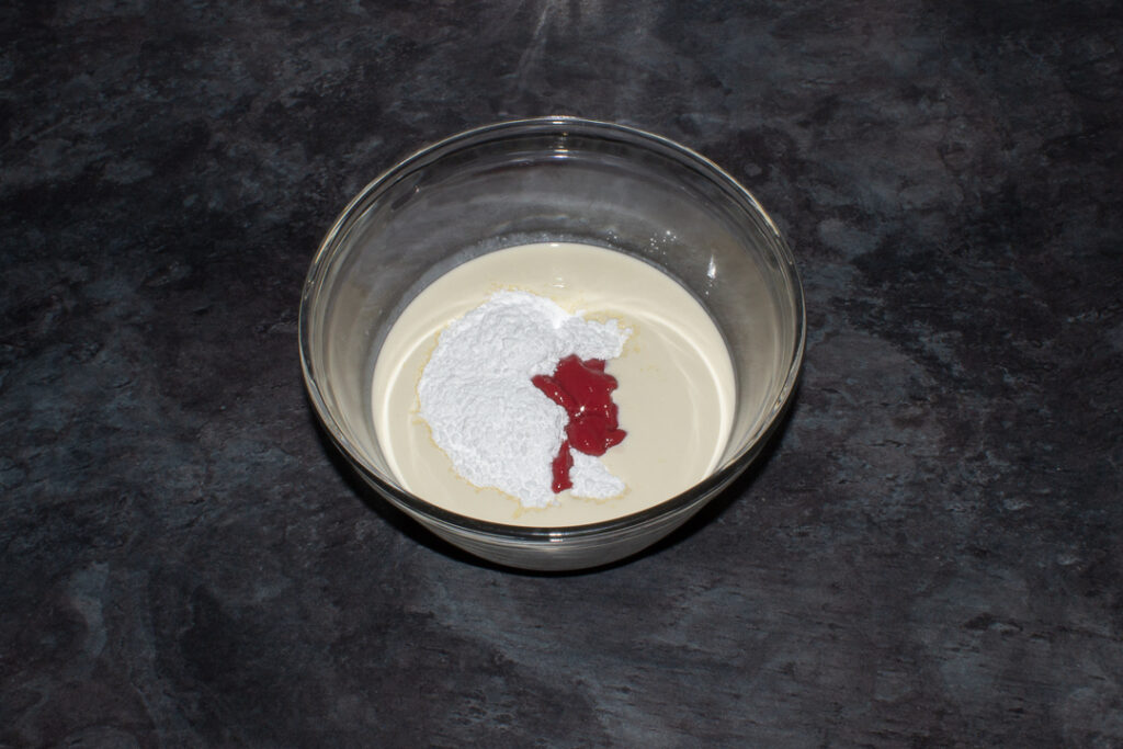 Cream, strawberry puree and icing sugar in a bowl.
