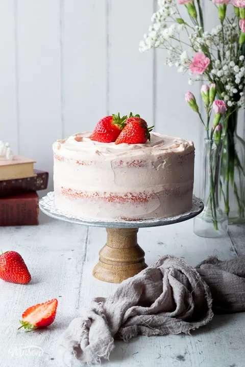 A whole strawberry cake on a stand with flowers