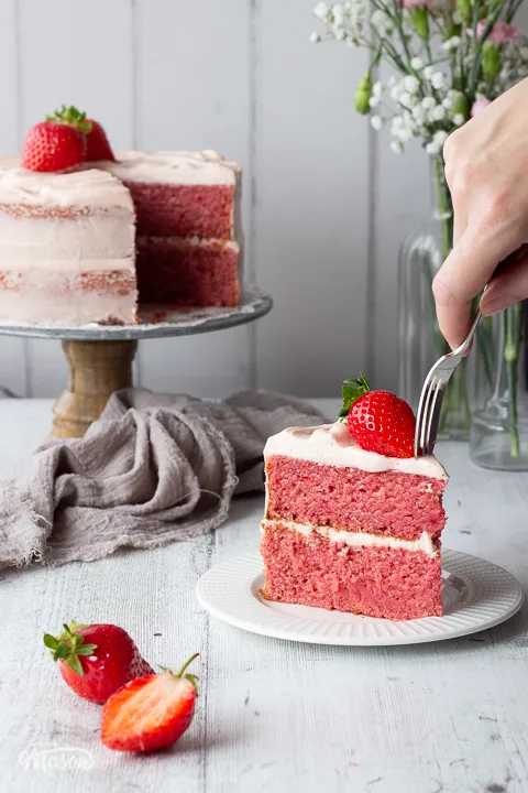 Someone pushing a fork into a slice of strawberry cake