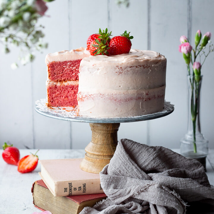 A strawberry cake with a slice cut out on a cake stand