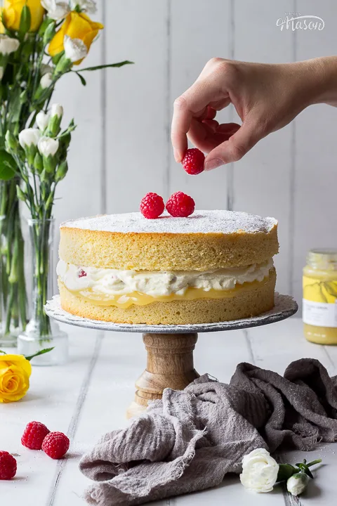 Someone placing a raspberry on top of a raspberry and lemon cake.