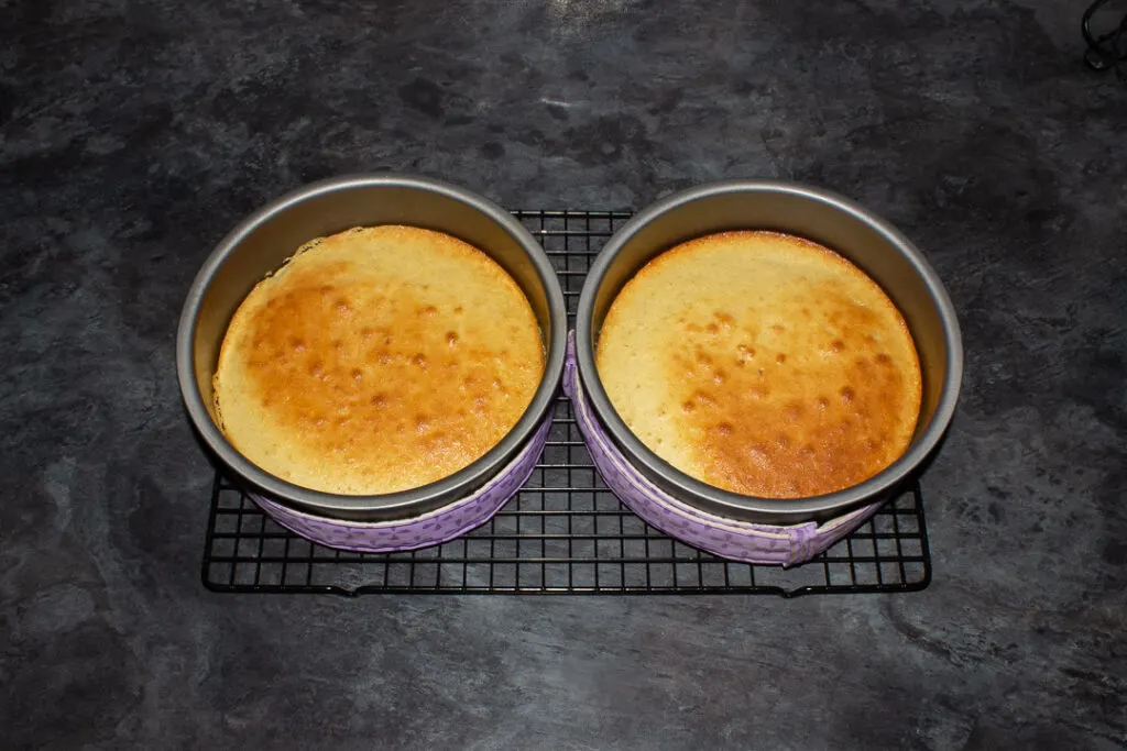 Two lemon cakes in tins on a cooling rack.