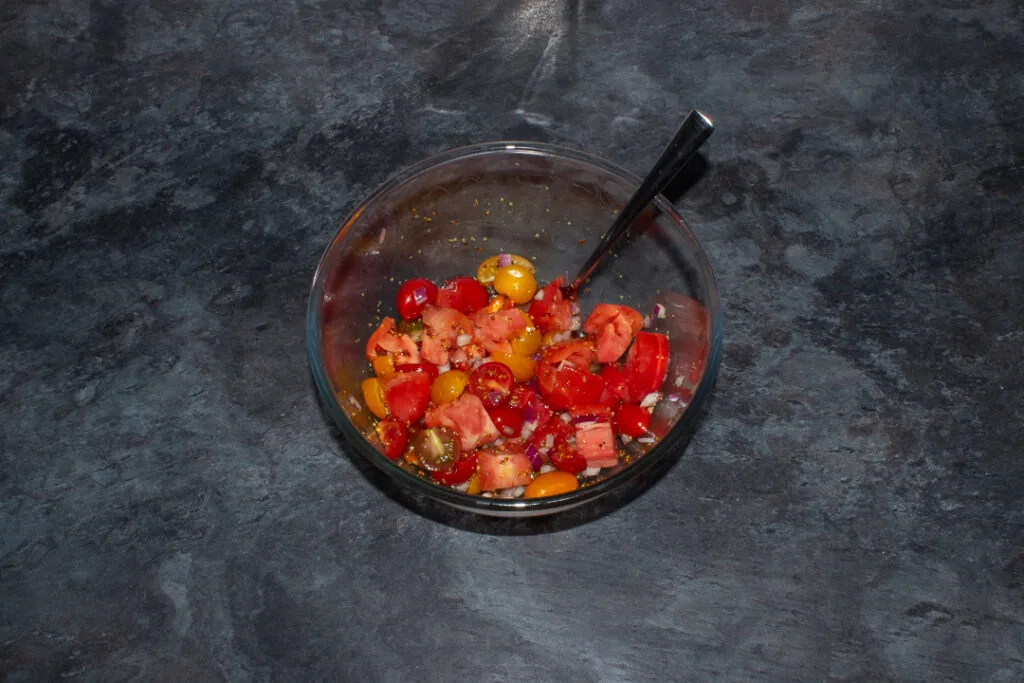 Diced onion, tomatoes and dressing in a mixing bowl