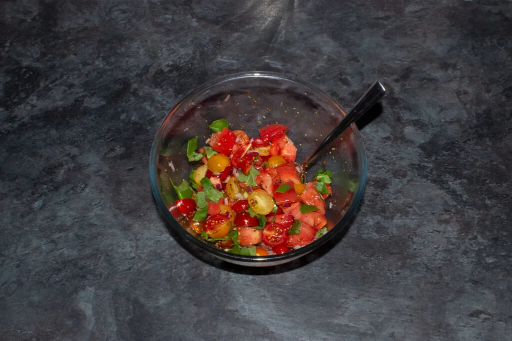 Tomato salad in a glass mixing bowl with a spoon