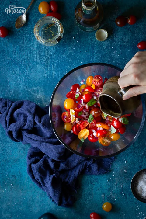 Someone pouring a dressing over a bowl of tomato salad