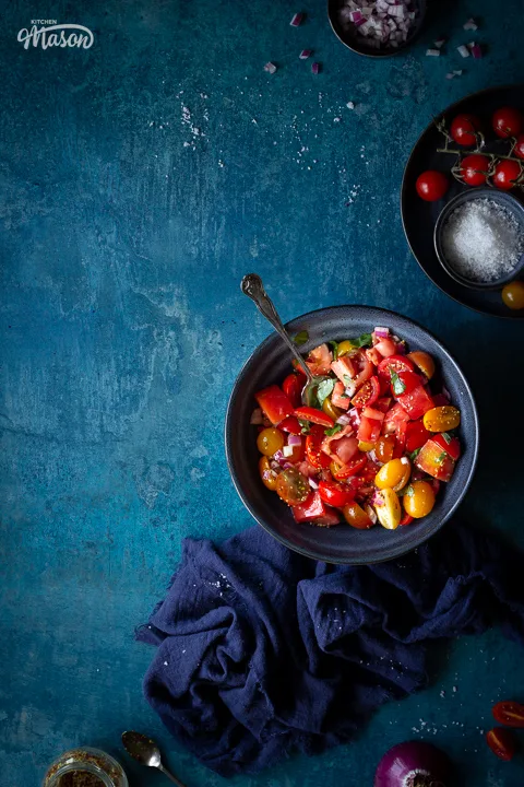 Tomato salad in a blue bowl with a spoon