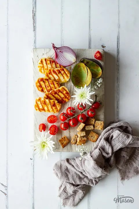 A wooden board filled with halloumi and vegetables