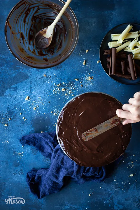 Someone covering biscuit cake with chocolate ganache