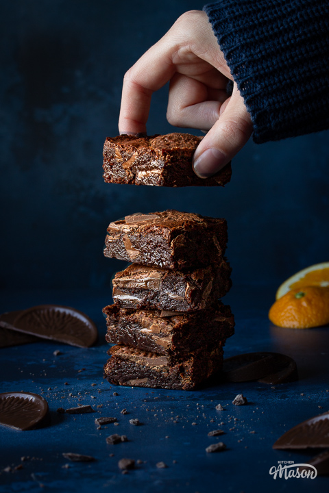 Someone taking a Terry's chocolate orange brownie off the top of a stack