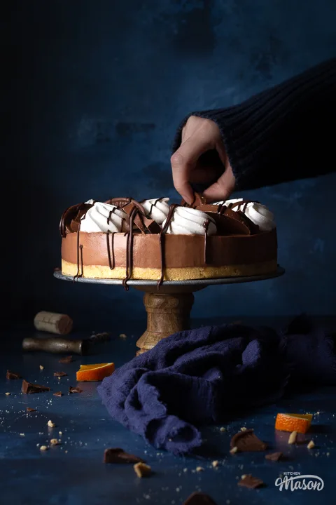 Someone decorating a no bake chocolate orange cheesecake on a cake stand