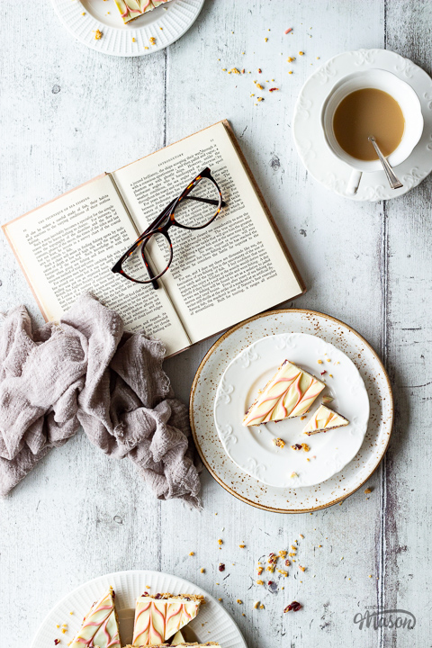 A slice of white chocolate tiffin on a plate next to a book and a pair of glasses