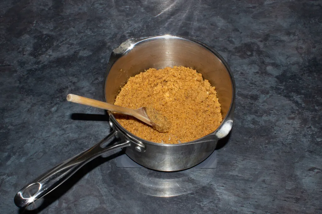 Biscuit crumbs mixed with a butter syrup in a saucepan