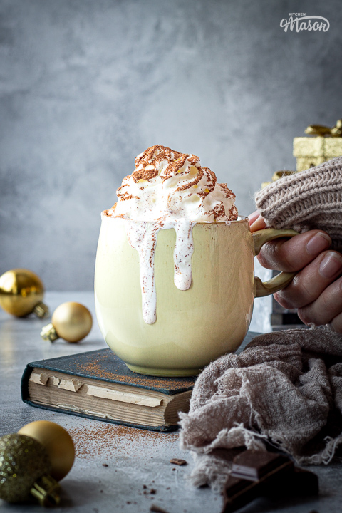 Someone holding a mug of festive hot chocolate with cream dripping down the sides