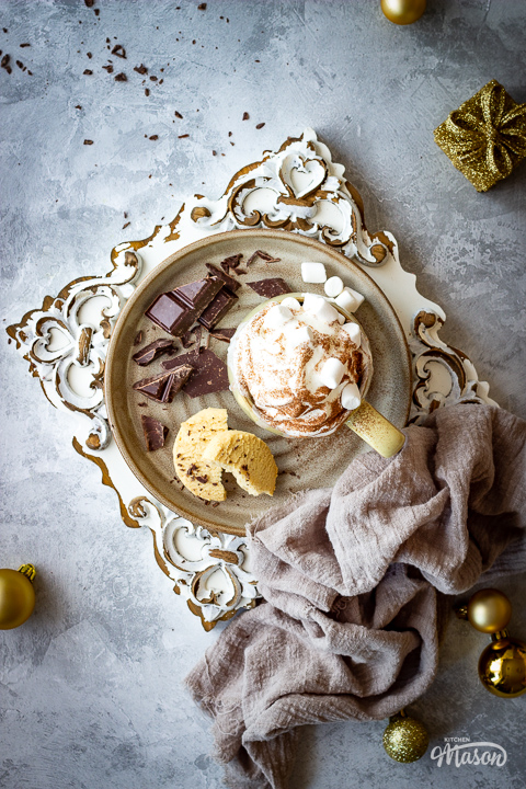 A plate with broken chocolate, biscuits and festive hot chocolate.