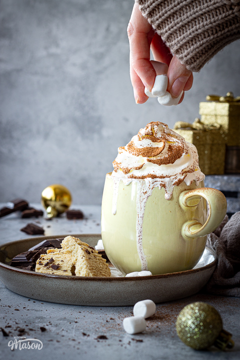 Someone topping a festive hot chocolate with marshmallows