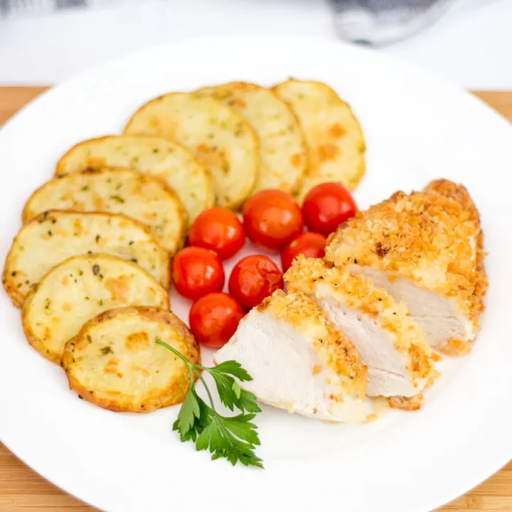 Baked parmesan chicken, potato thins and tomatoes on a white serving plate
