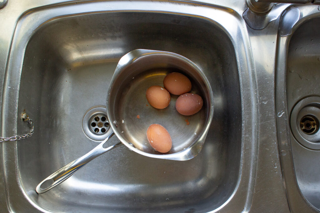 4 eggs in a saucepan in the sink. The shells are broken.