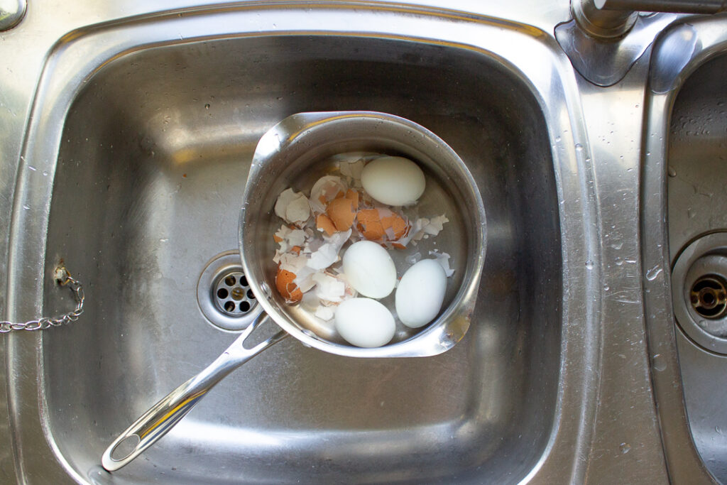 4 peeled eggs and their shells in a pan of cold water