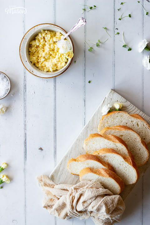A board with sliced bread and a small bowl of egg salad