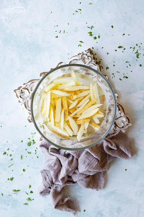 French fries soaking in a bowl of water on a decorative board
