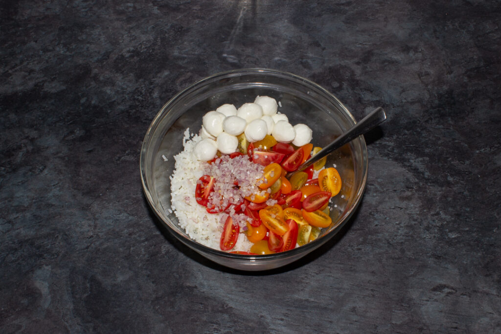Cooked rice, tomatoes, shallots, and mozzarella pearls in a bowl