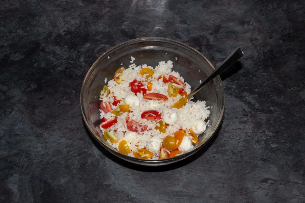 Cooked rice, tomatoes, shallots, and mozzarella pearls mixed together in a large bowl