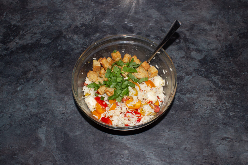 Croutons and torn basil leaves added to a rice and tomato salad in a mixing bowl