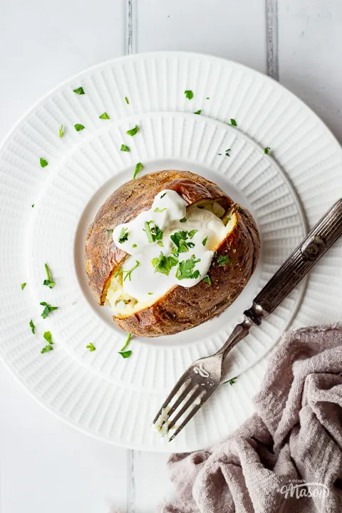 A close up of a Ninja air fryer jacket potato on a plate topped with soured cream.