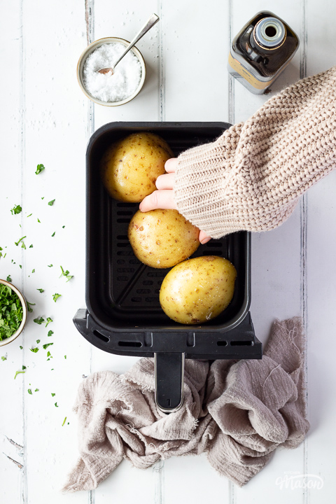 Someone placing an oiled and salted potato into an air fryer drawer