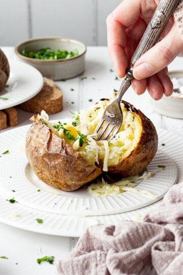 Someone forking a Ninja air fryer jacket potato with cheese on a white plate